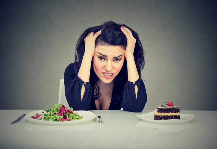 Image of a woman fighting the craving to eat cake when she should be eating salad. 