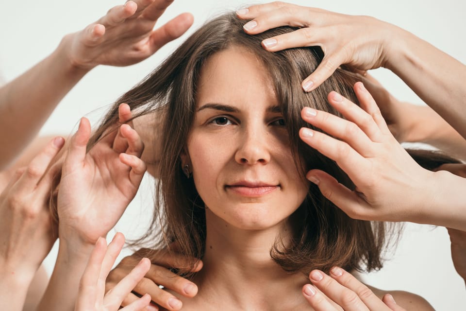 Woman having boundaries violated by hands of multiple people, looks unhappy.