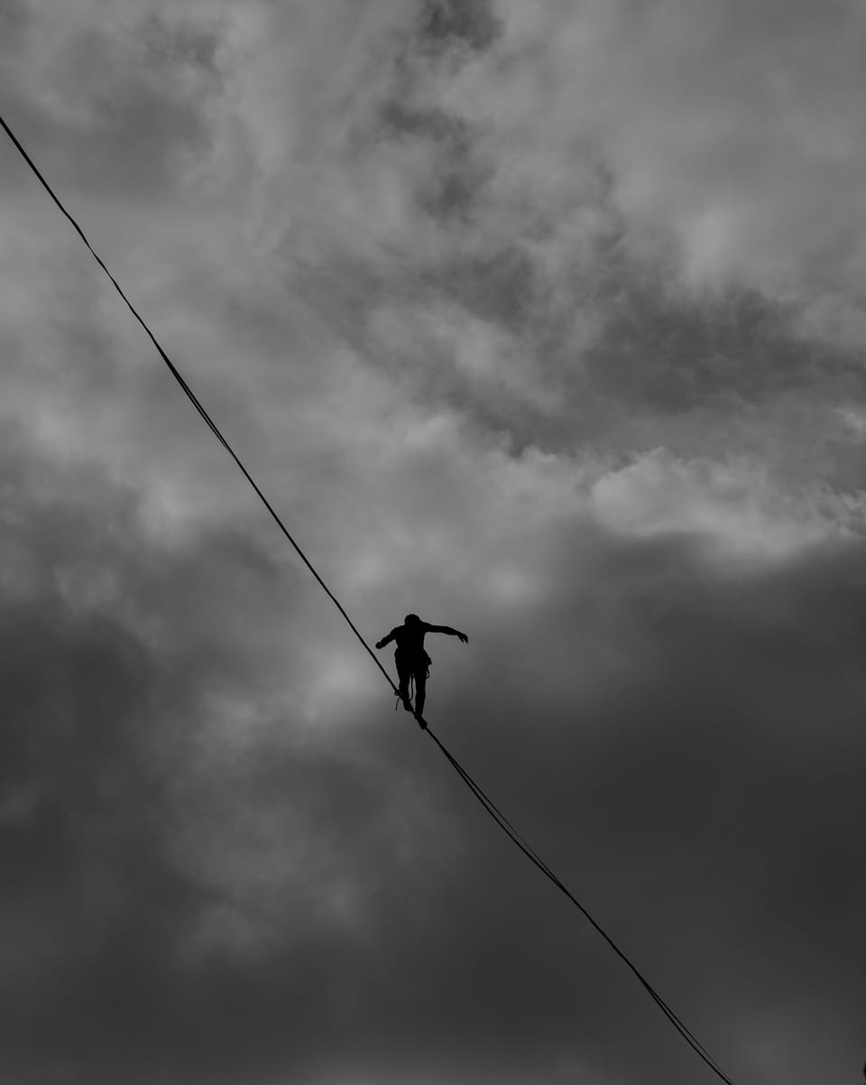 Image of a tightrope walker in the sky walking across a wire. 